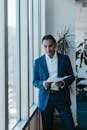 Confident business professional in suit holding documents in a bright office environment.